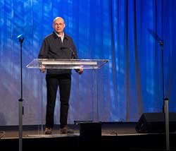 The rise and fall prompter stand is below the front edge of the stage and keeps the stage clear. This allows the mirrors to drop a little lower and give the video director a clear shot of the stage.