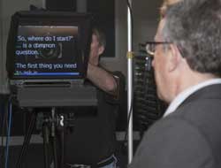 This presenter is working with an on-camera prompter. If you look closely, you can see the camera lens behind the prompter mirror.